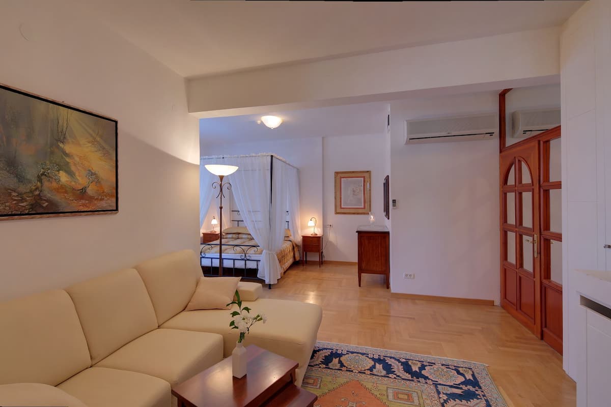 Una sala de estar con un sofá color beige, un cuadro, un televisor y suelo de madera.