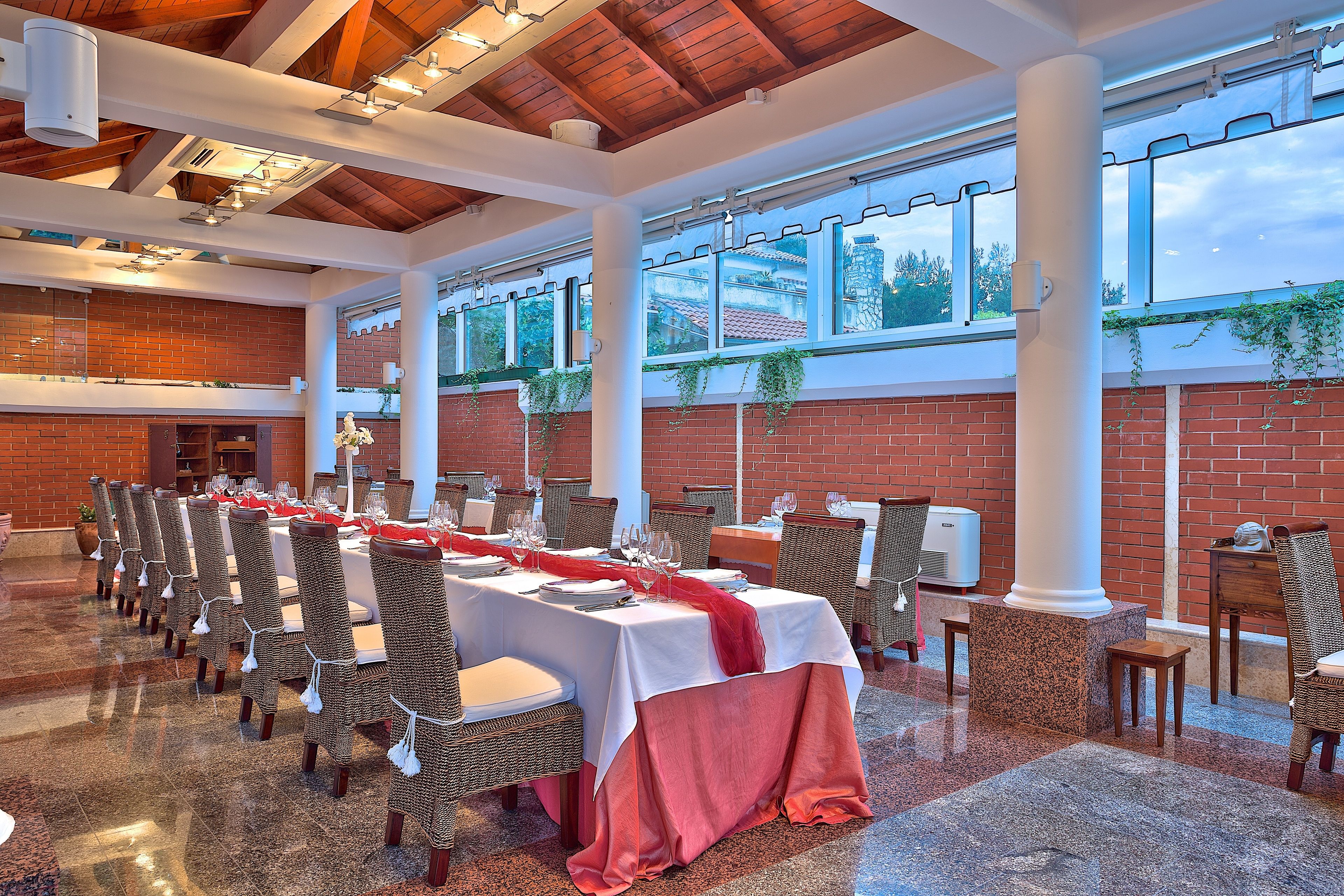 A banquet hall with long tables set for dining, surrounded by wicker chairs.