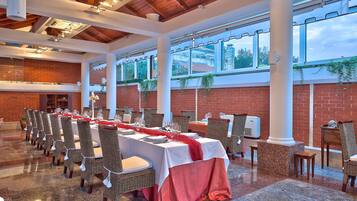 A banquet hall with long tables set for dining, surrounded by wicker chairs.