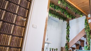 A library with bookshelves, a staircase with greenery, and a wooden ceiling. - B&B Tecla (Naples)