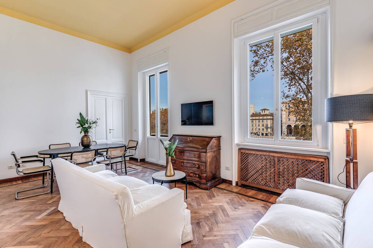 A spacious living room with a large window, a dining area with a round table, and a cozy seating arrangement.