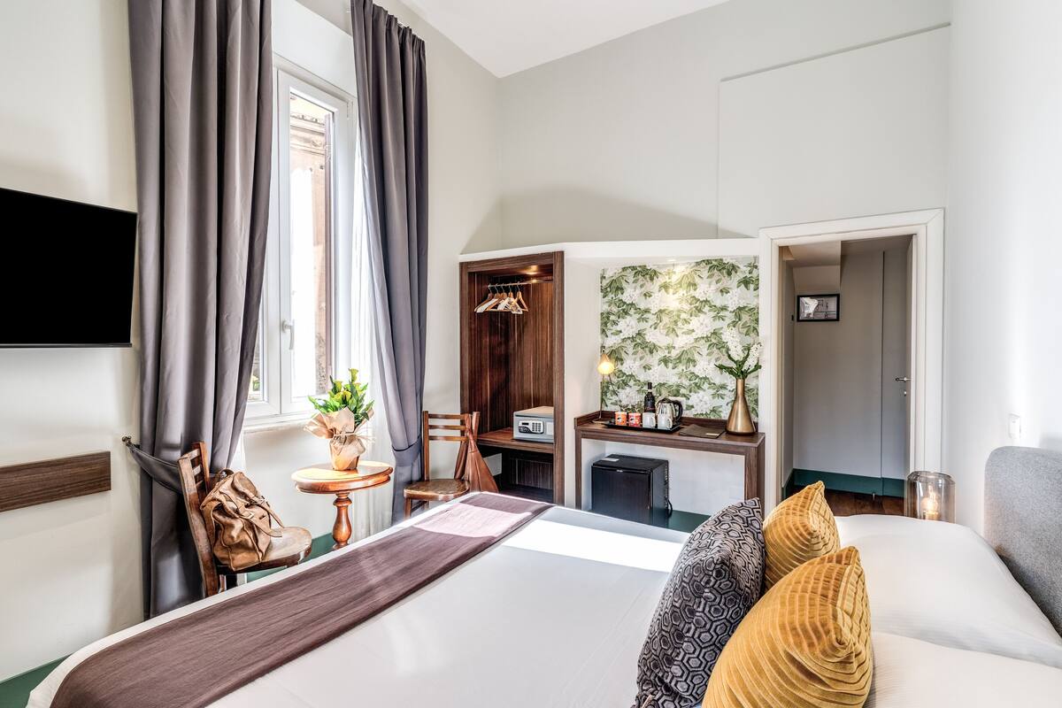 A hotel room with a bed, a desk, a chair, a TV, and a view of the outside.