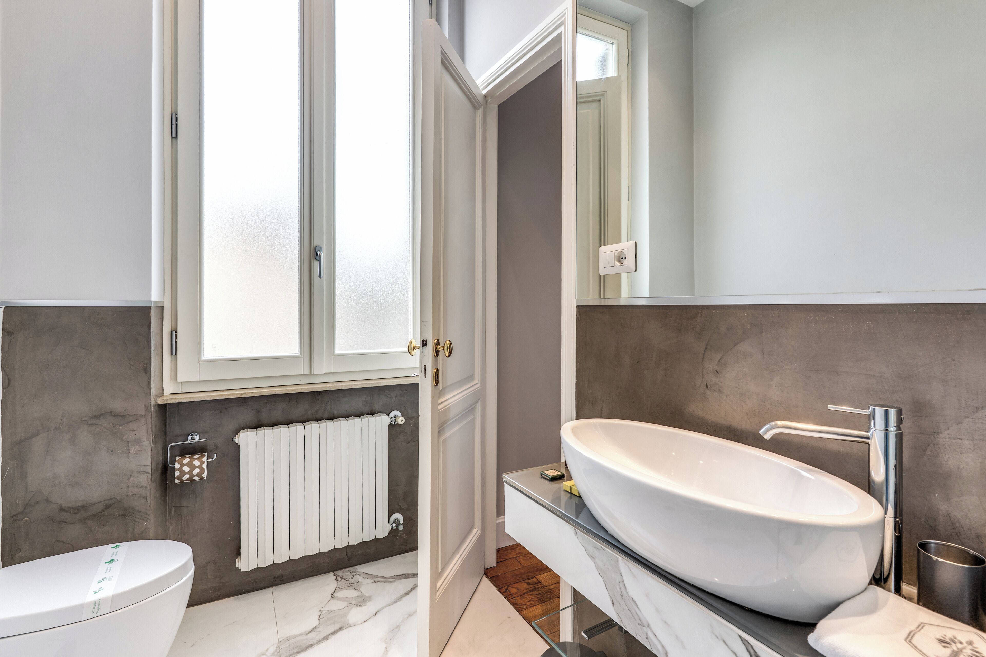 A modern bathroom with a large oval sink, a toilet, a towel rack, and a mirror.