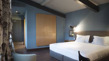 A bedroom with a large bed, a wardrobe, a chair, and a nightstand with a lamp.