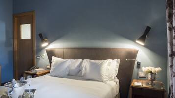 Habitación de hotel con cama, mesitas de noche, lámpara y un jarrón con flores.