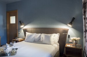 A hotel room with a bed, bedside tables, a nightstand, a lamp, and a vase with flowers.