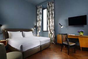 A modern hotel room with a large bed, a desk, a chair, a TV, and a window with curtains.