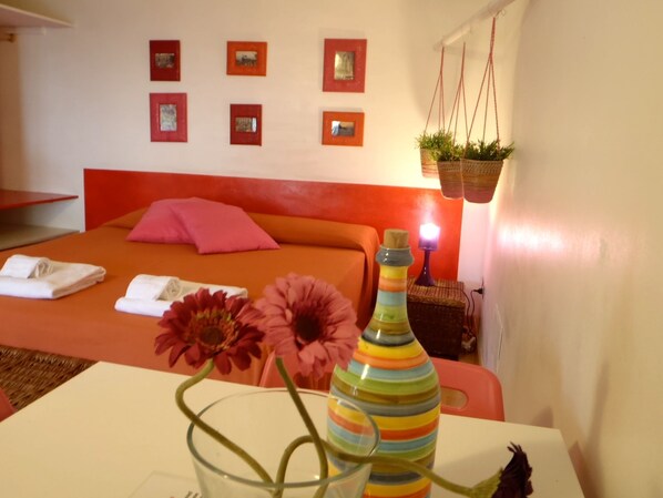 Een hotelkamer met een bed, kussens, een nachtkastje met een vaas en een wand met ingekaderde foto's.