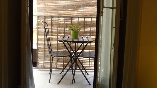 An open door leading to a balcony with a metal table and chairs, a potted plant, and a bamboo fence. - Gianluca Rooms (Catania)