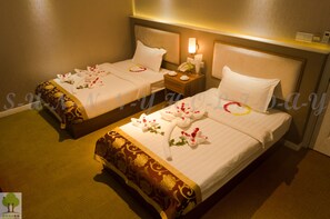 Two hotel beds with floral bedspreads and towels, a bedside table with a lamp, and a wall-mounted telephone. - Sunny Holiday Hotel (Yangon)