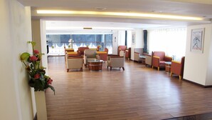 A spacious lobby with wooden flooring, multiple seating areas, and a large window with a view. - Sunny Holiday Hotel (Yangon)