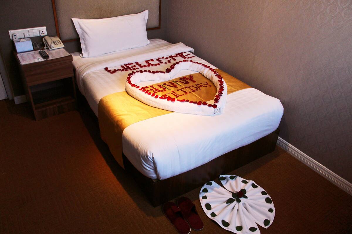 A neatly made bed with a heart-shaped decoration on the bedspread and a towel with a heart design on the floor.