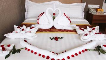 A hotel room with a bed featuring a decorative swan and rose arrangement, a bedside table with a telephone and a box, and a wall socket.