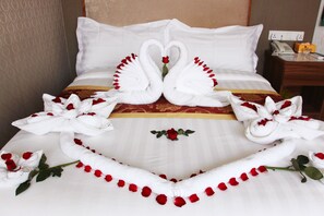 A hotel room with a bed featuring a decorative swan and rose arrangement, a bedside table with a telephone and a box, and a wall socket. - Sunny Holiday Hotel (Yangon)