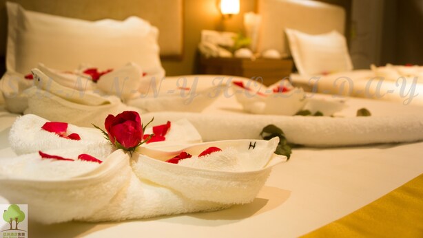 A hotel room with neatly arranged towels, a bed with white bedding, and a bedside table with a lamp. - Sunny Holiday Hotel (Yangon)