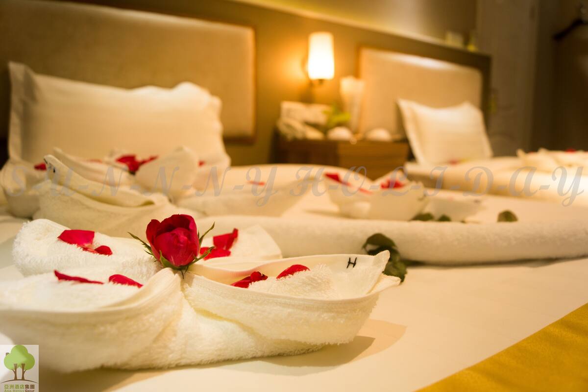 A hotel room with neatly arranged towels, a bed with white bedding, and a bedside table with a lamp.