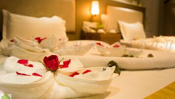 A hotel room with neatly arranged towels, a bed with white bedding, and a bedside table with a lamp.