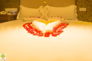 A bed with a heart-shaped arrangement of white towels and red rose petals. - Sunny Holiday Hotel (Yangon)
