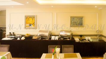 A buffet setup with various food items and utensils, a vase with flowers, and framed artwork on the wall.