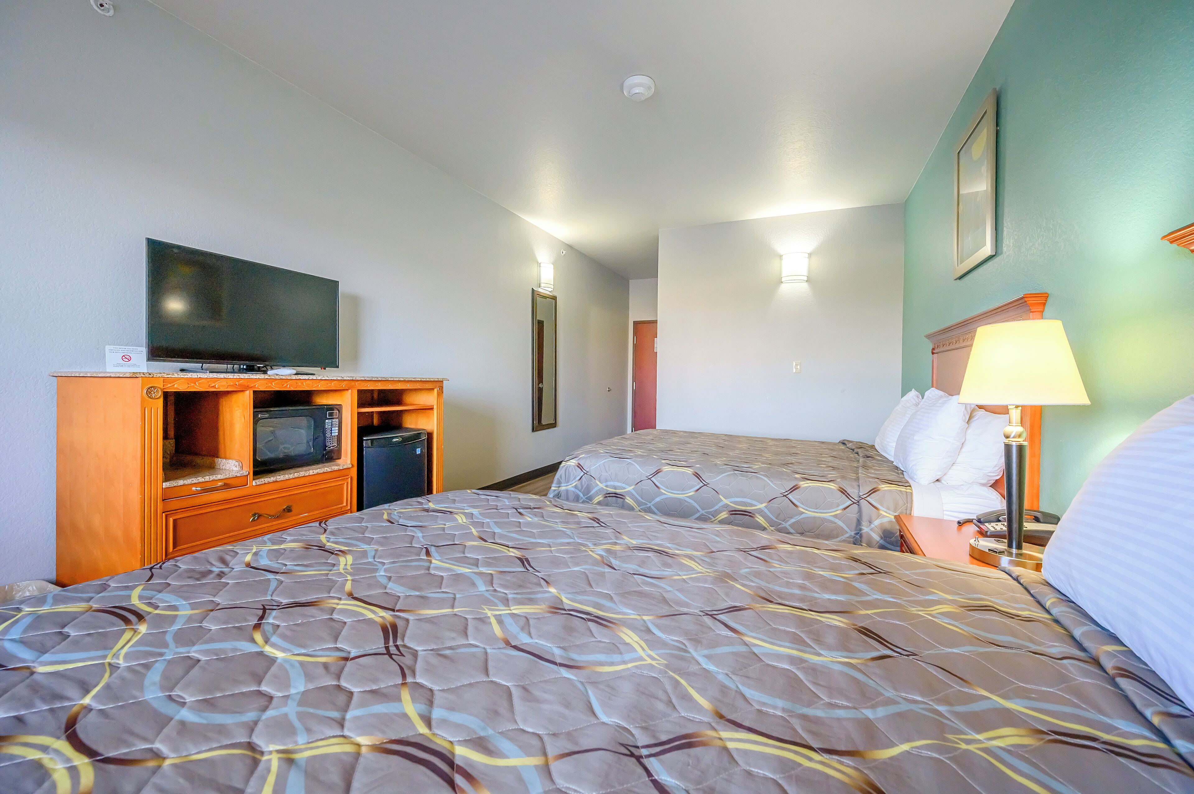 Een hotelkamer met een bed, een televisie, een bureau met lamp en een magnetron.