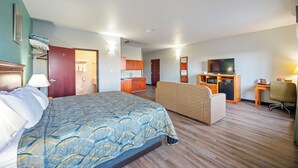Una habitación de hotel con una cama grande, un sofá, un escritorio, un televisor y una kitchenette.
