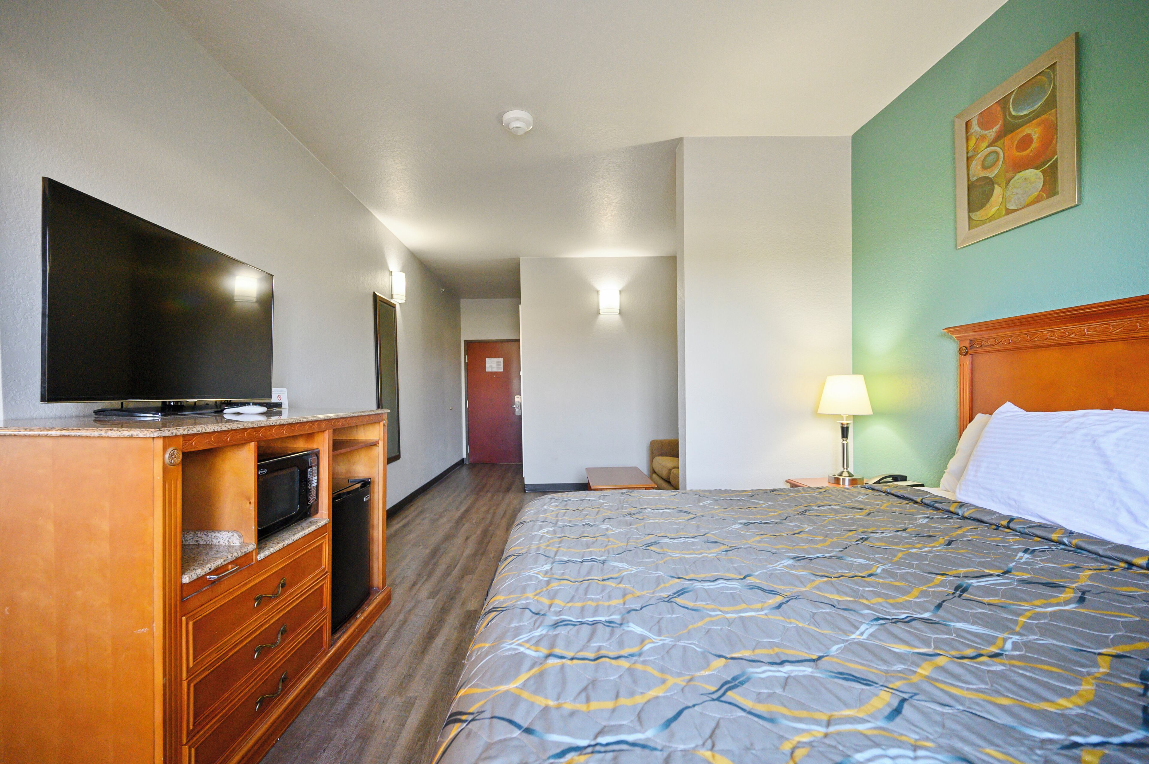 A hotel room with a bed, a television, a microwave, and a wooden cabinet.