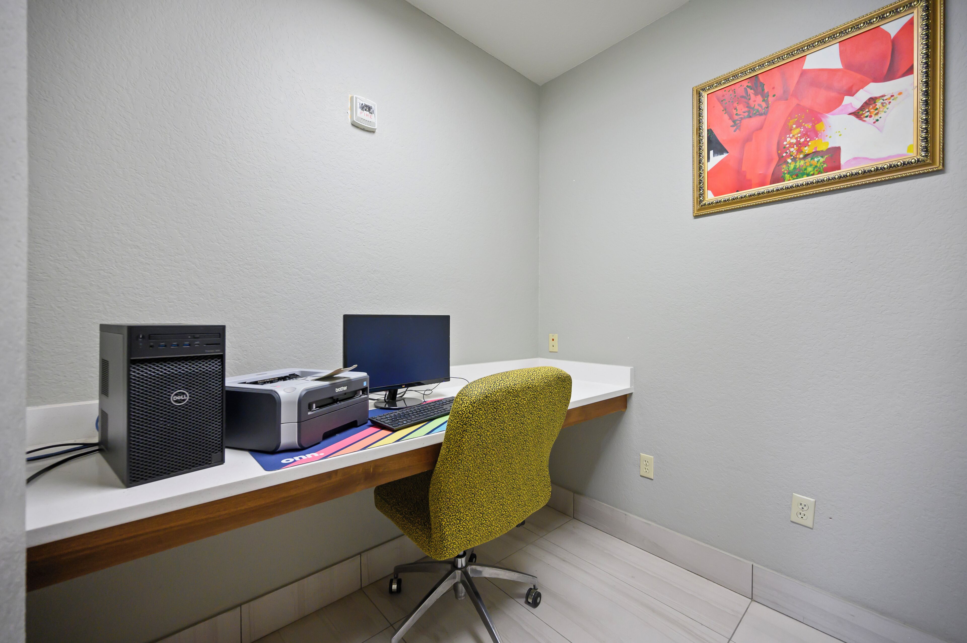 Uma mesa de escritório com um computador, impressora e teclado. Há uma cadeira em frente à mesa.