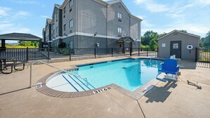 A swimming pool with a 3ft 6in depth, a covered seating area, and a building with multiple windows and a sign indicating a hazardous materials storage area.