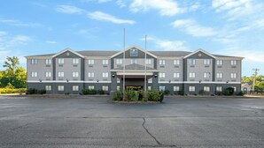 A multi-story hotel with a central entrance, a parking lot, and a clear sky.