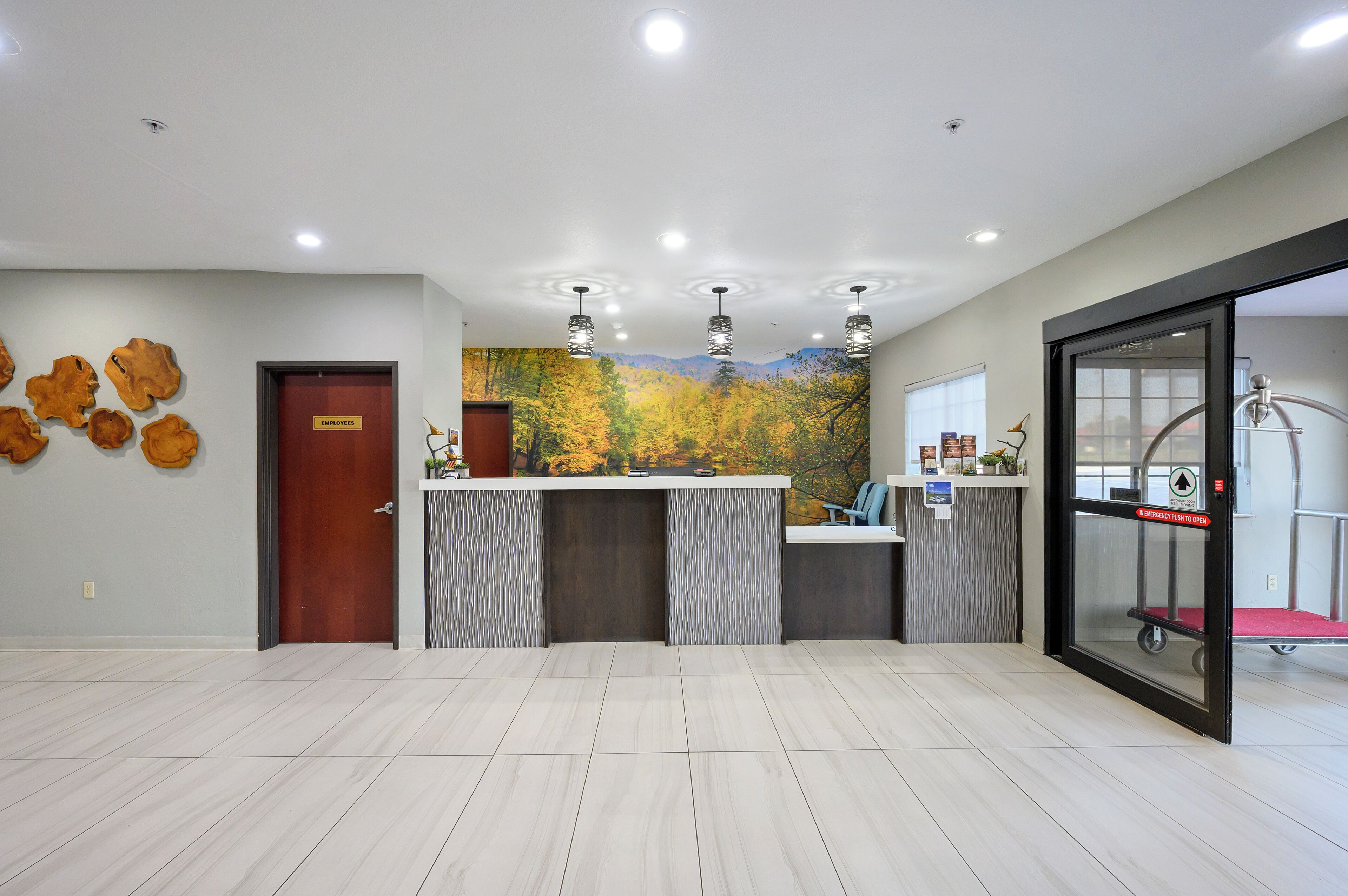 A reception area with a wooden door, a reception desk, a mural of autumn leaves, and a glass elevator.