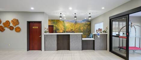 A reception area with a wooden door, a reception desk, a mural of autumn leaves, and a glass elevator.