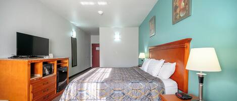 Ein Hotelzimmer mit einem Bett, einem Fernseher, einer Holzkommode und einem Nachttisch mit Lampe.