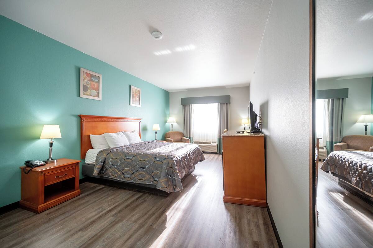A hotel room with a bed, bedside tables, a dresser, and a large mirror.
