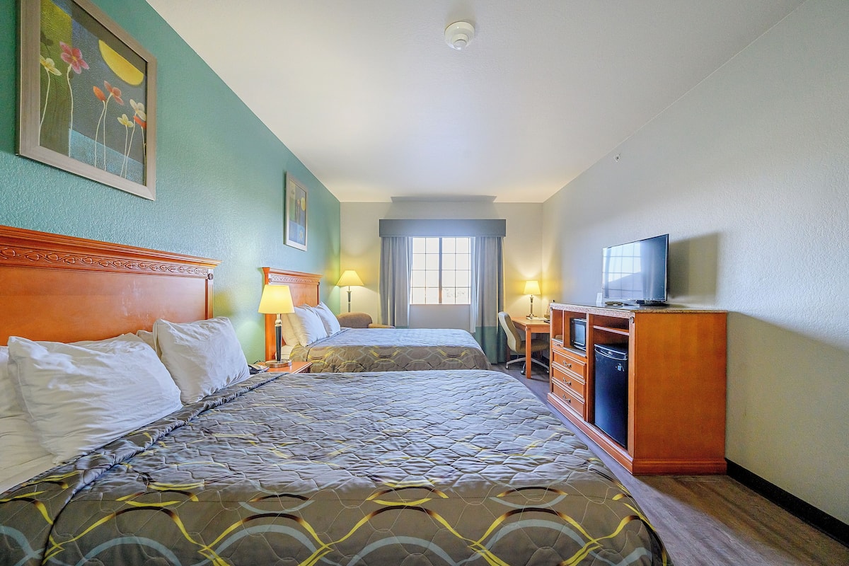 A hotel room with two beds, a desk, a television, and a window.