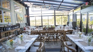A restaurant with a long table set for a meal, surrounded by chairs, and a wine rack with bottles. - Jedediah Hawkins Inn (Jamesport)