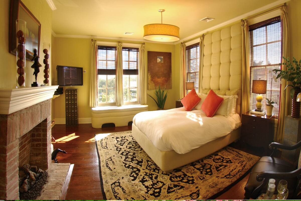 A bedroom with a large bed, a fireplace, a television, and a window with curtains.
