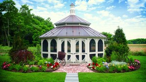 A gazebo with a dome roof, surrounded by a garden with various flowers and a pathway leading to it. - Jedediah Hawkins Inn (Jamesport)