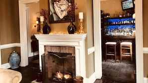 A cozy living room with a fireplace, a bar area with bottles, and a painting on the wall. - Jedediah Hawkins Inn (Jamesport)