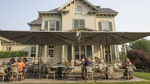 An outdoor patio area with tables and chairs, a covered seating area, and a large house in the background. - Jedediah Hawkins Inn (Jamesport)