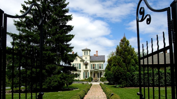 A brick pathway leading to a large, two-story building with a symmetrical facade, surrounded by manicured hedges and trees. - Jedediah Hawkins Inn (Jamesport)