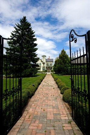 A brick pathway leading to a large, two-story building with a symmetrical facade, surrounded by manicured hedges and trees. - Jedediah Hawkins Inn (Jamesport)