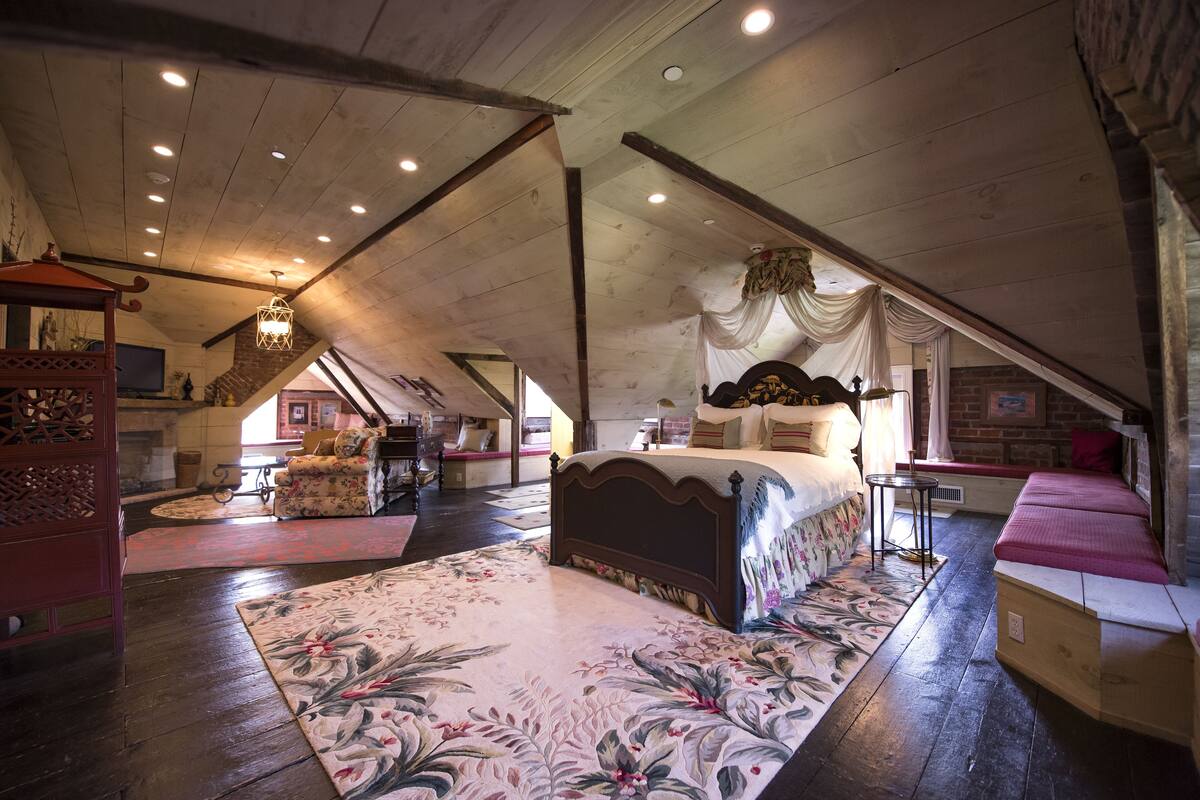 A spacious attic bedroom with a large bed, wooden beams, and a sloped ceiling.