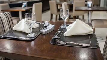 A dining table set with two place settings, each with a napkin, a glass, and cutlery.