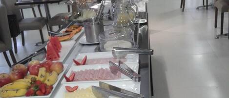 Montaje tipo buffet con diferentes alimentos y bebidas, como frutas, carnes y salsas.