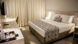 Una habitación de hotel con una cama grande, una mesita de noche, un televisor y una cortina.