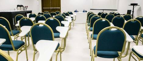A conference room with rows of chairs and tables, a podium, and a projector screen.