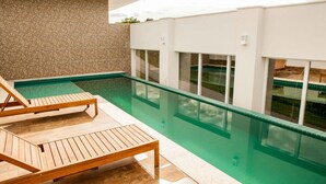 Zona de piscina exterior moderna con tumbonas de madera y una vista despejada de la piscina.