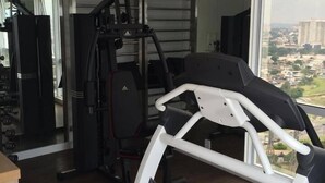 Un gimnasio con equipamiento cardiovascular, máquinas de pesas y vistas a un paisaje urbano a través de amplias ventanas.