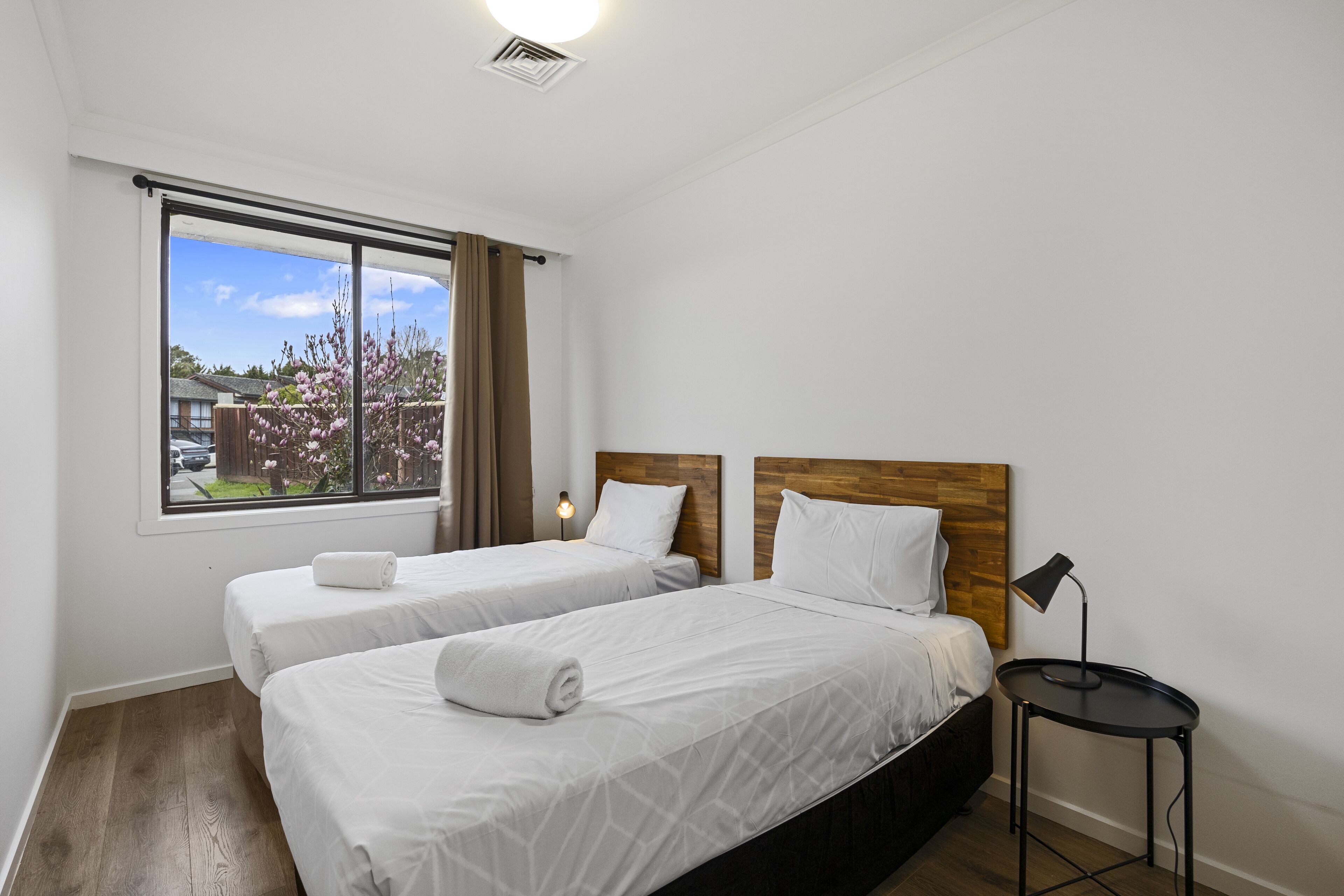 Habitación de hotel con dos camas, cabecero de madera, una mesita con lámpara y una ventana con cortinas.