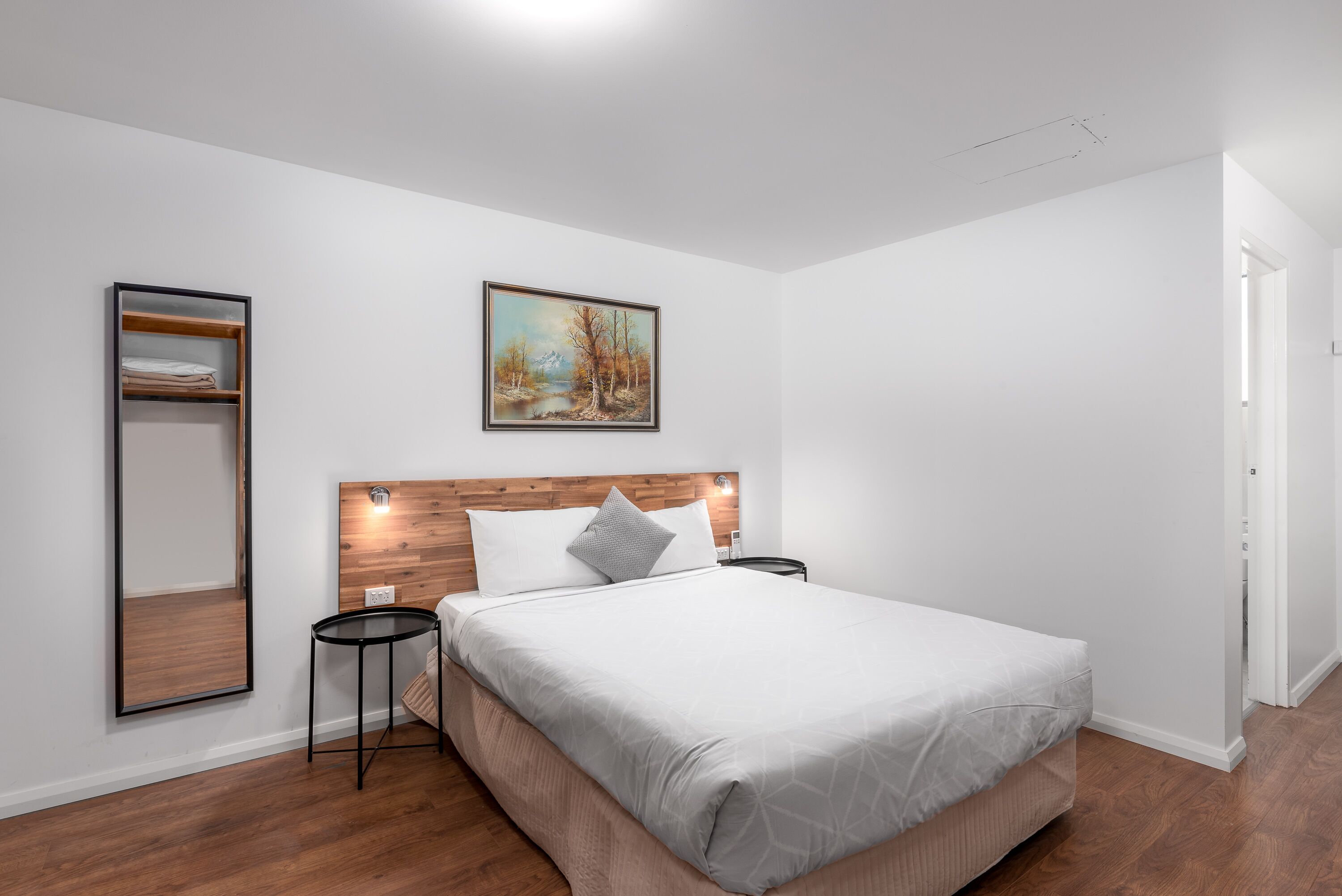Une chambre moderne avec une tête de lit en bois, un grand lit, une table de chevet, un miroir et un tableau accroché au mur.
